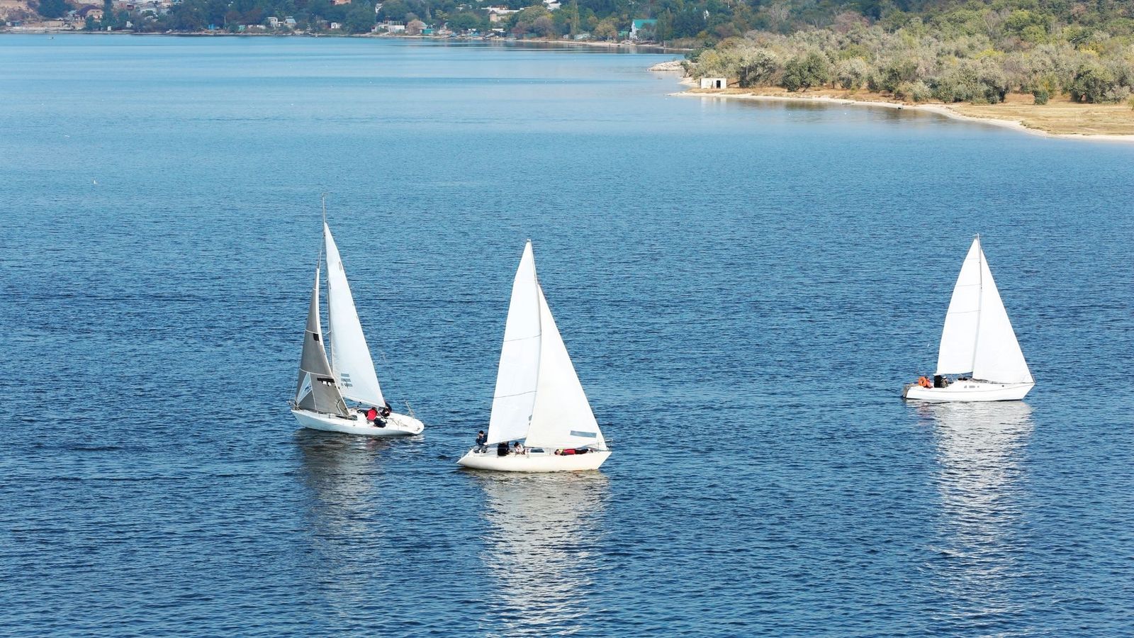 Tres veleros navegando juntos por un embalse en calma